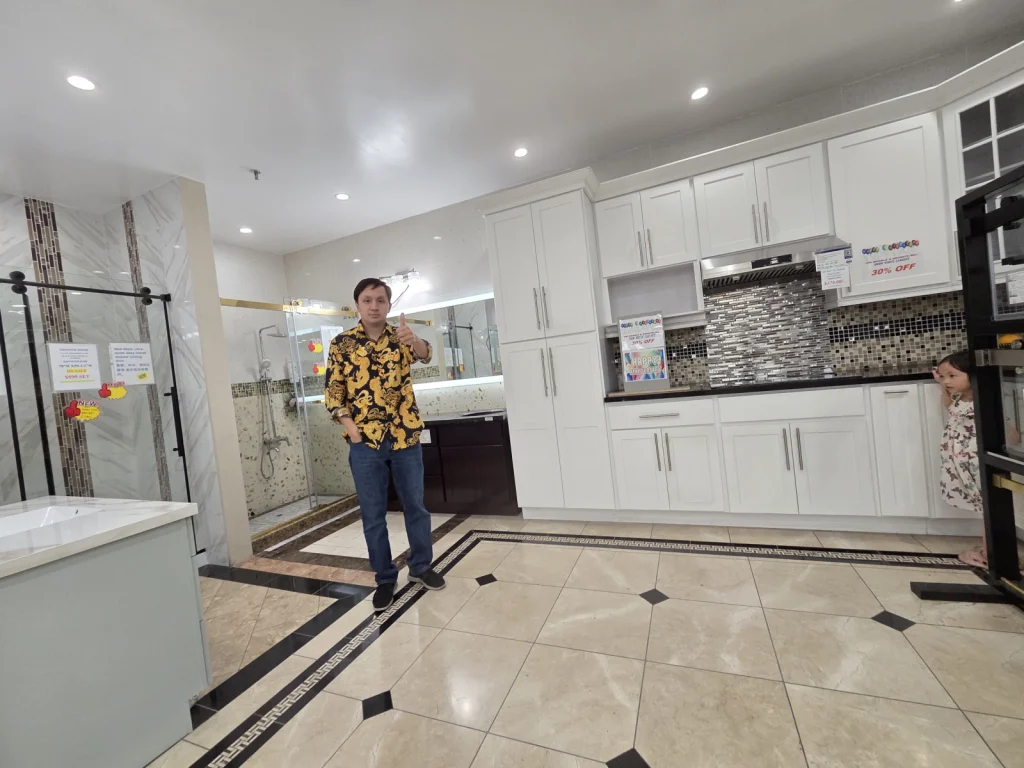 Tommy Nguyen, CEO of 9Builders, posing with a thumbs-up in a showroom at Unimarble, featuring a kitchen and bathroom display.