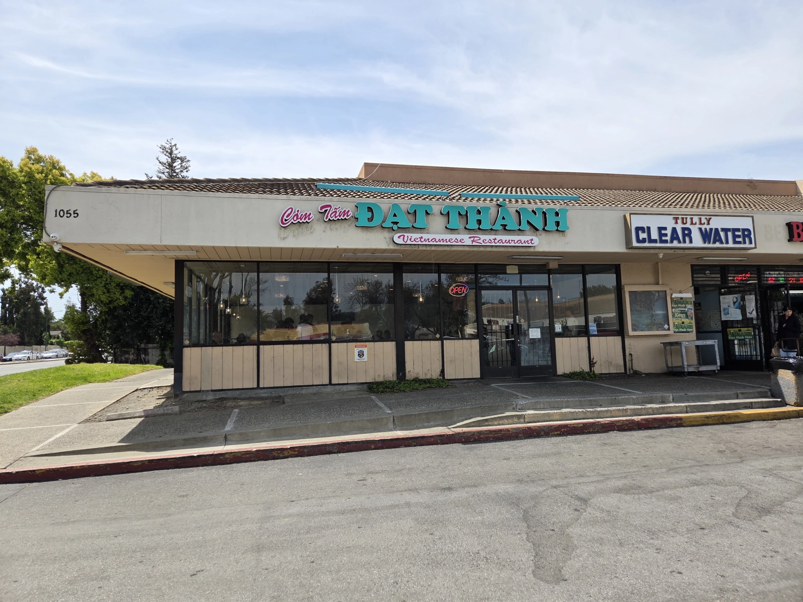 The exterior of Com Tam Dat Thanh, located at 1055 Tully Rd, San Jose, CA, featuring the restaurant's sign and a nearby business with a clear view of the surrounding area.
