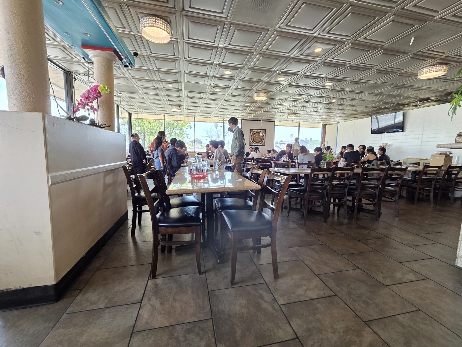 A wide view of the dining area at Com Tam Dat Thanh, showing multiple tables filled with customers. The ceiling design and large windows let in natural light, creating a bright and welcoming atmosphere.
